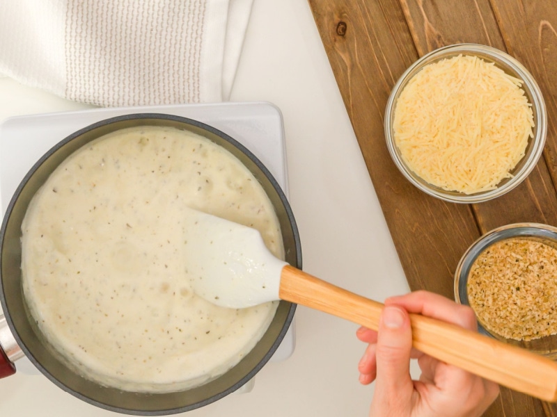 Heating Alfredo Sauce on a Pan with Parmesan Cheese to the Side