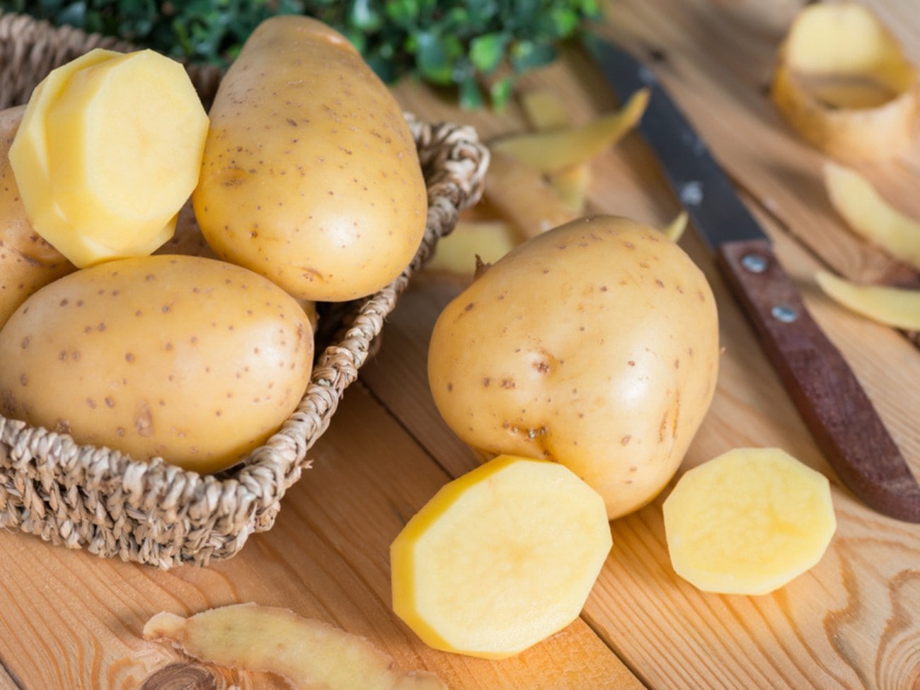 Whole Potatoes in a Basket with One Peeled and Sliced Potato on a Cutting Board with a Pairing Knife