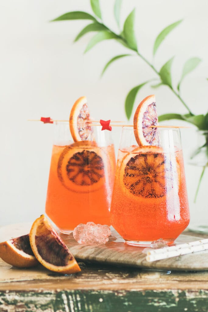 Two Glasses of Pink Whitney and Aperol with Blood Oranges on a Wooden Table