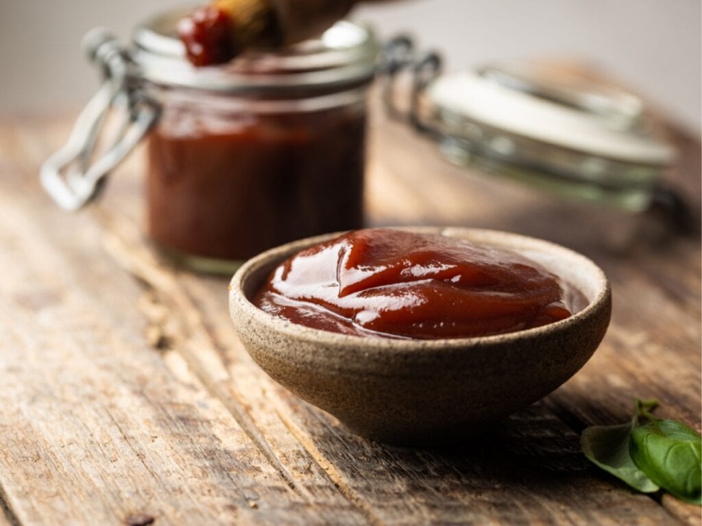 Barbecue Sauce In A Saucer With Basting Brush Over Rustic Barn Wood Table 