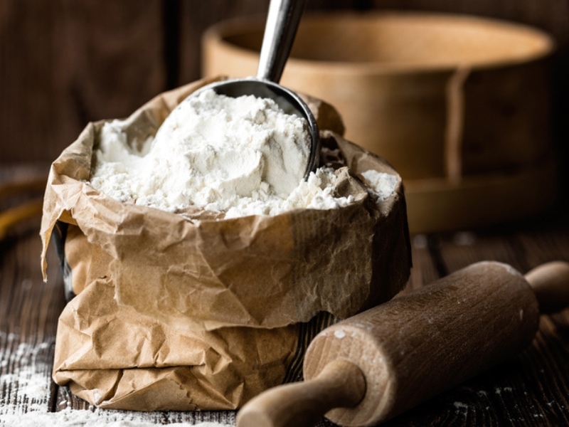 Brown Paper Bag of Cake Flour with Measuring Cup Full of Flour Sitting in the Bag and a Wooden Rolling Pin on the Side