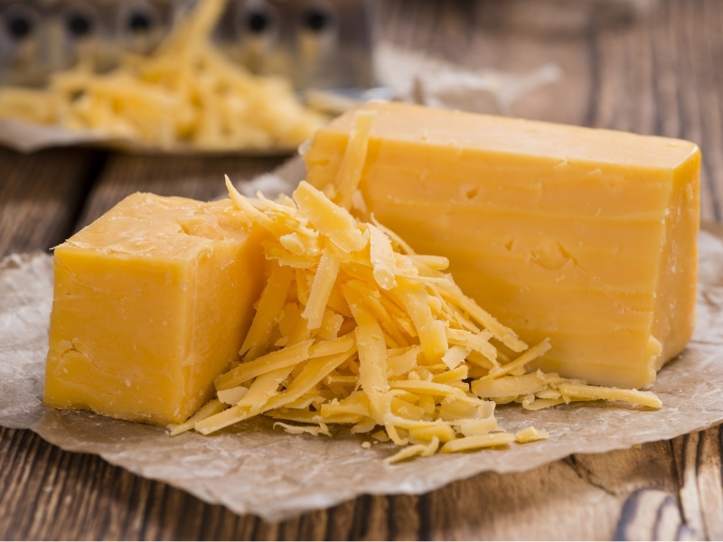 Whole and Grated Cheddar Cheese on a Parchment Paper