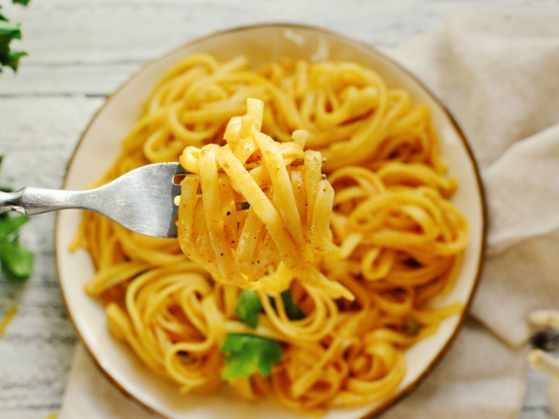 Bowl of Cooked and Seasoned Egg Noodles in a Large Bowl in the Background, with Egg Noodles Twirled Around a Fork in the Foreground Focus