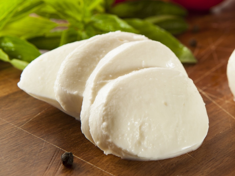 Slices of Mozzarella Cheese with Herbs and Spices on a Wooden Cutting Board