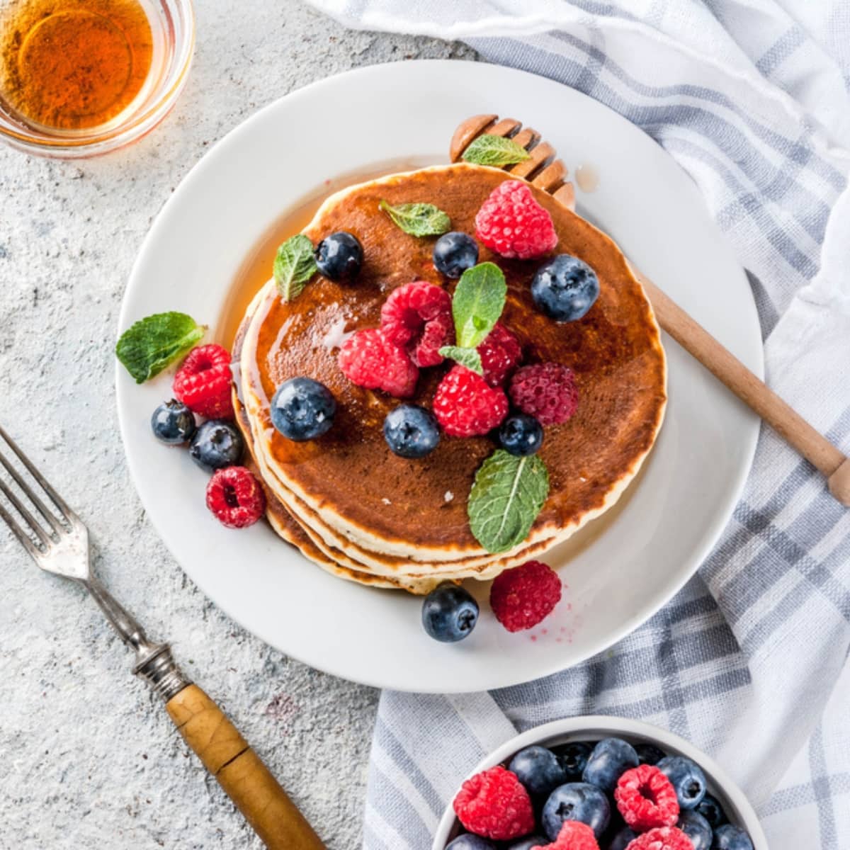 Oat flour pancake top view on a plate topped with fresh berries drizzled with syrup and a bowl of berries on the side with a fork.