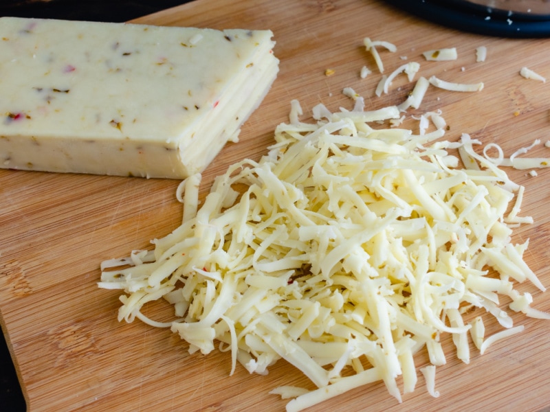 Whole and Grated Pepper Jack Cheese on a Wooden Cutting Board