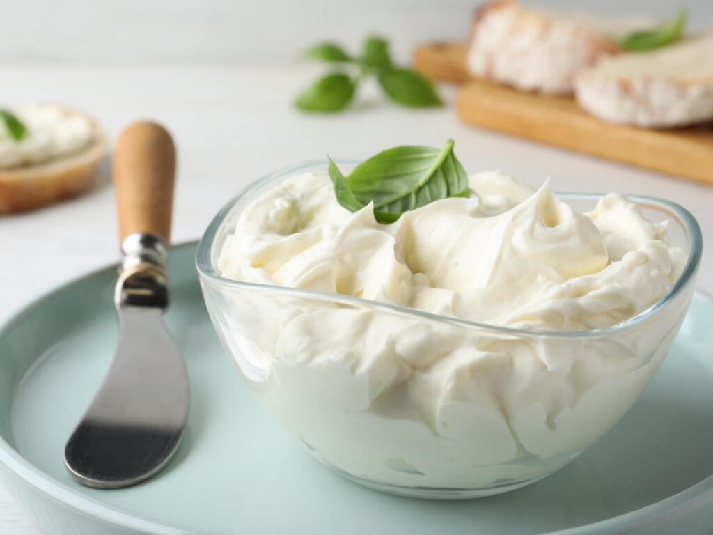 Glass bowl with vegan cream cheese on a plate with a butter knife
