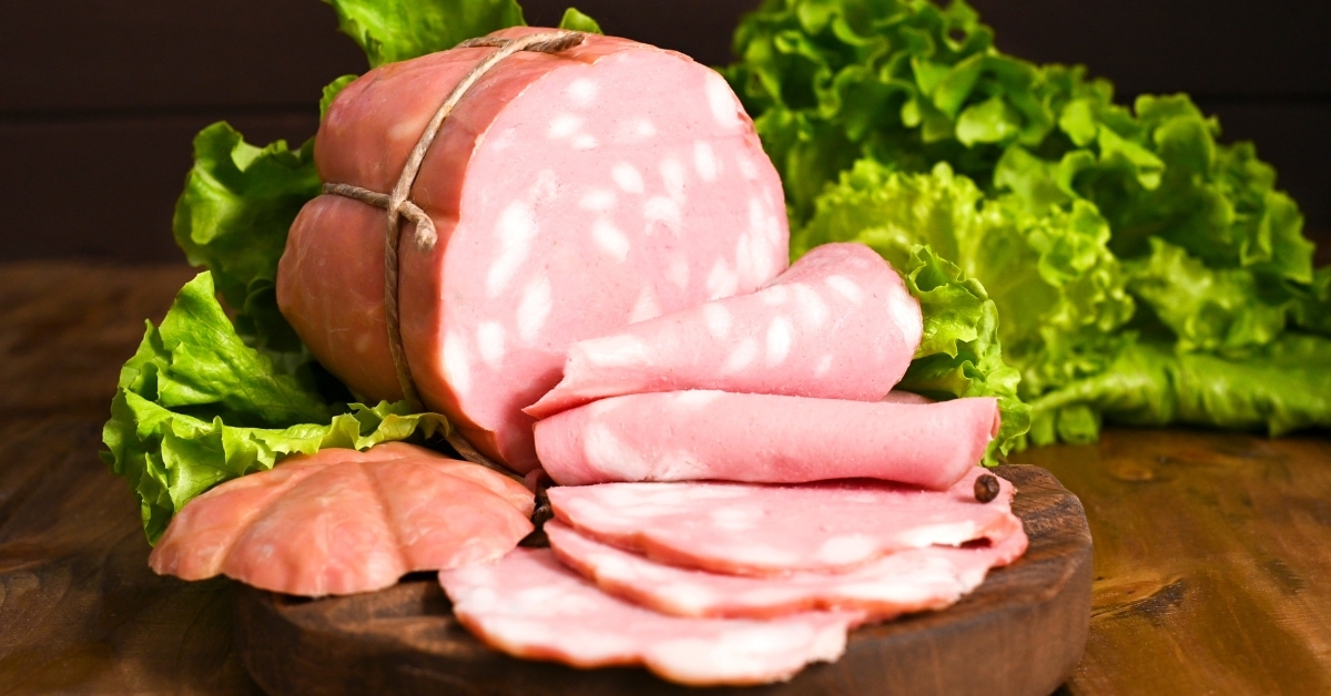 Whole Block of Mortadella Sliced in a Wooden Cutting Board with Lettuce