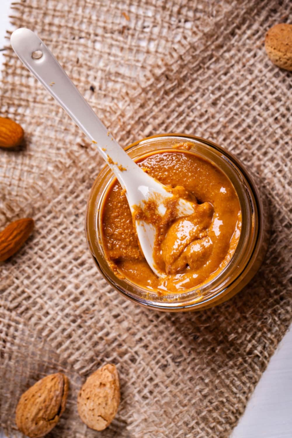 Jar of Homemade Almond Butter Top View with a Spoon on a Burlap Cloth