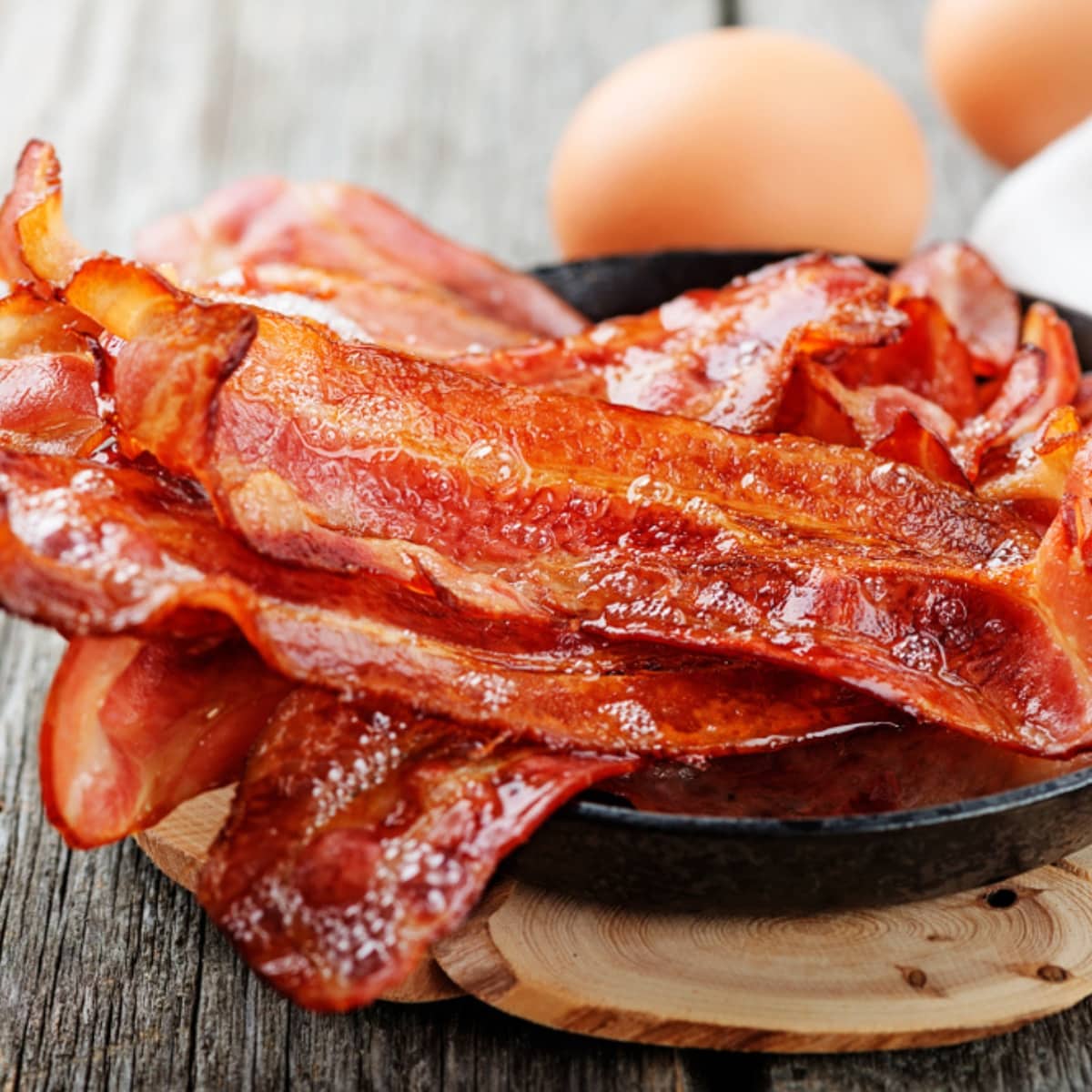 Baked Bacon Strips on a Serving Plate with Hard-Boiled Eggs in the Background