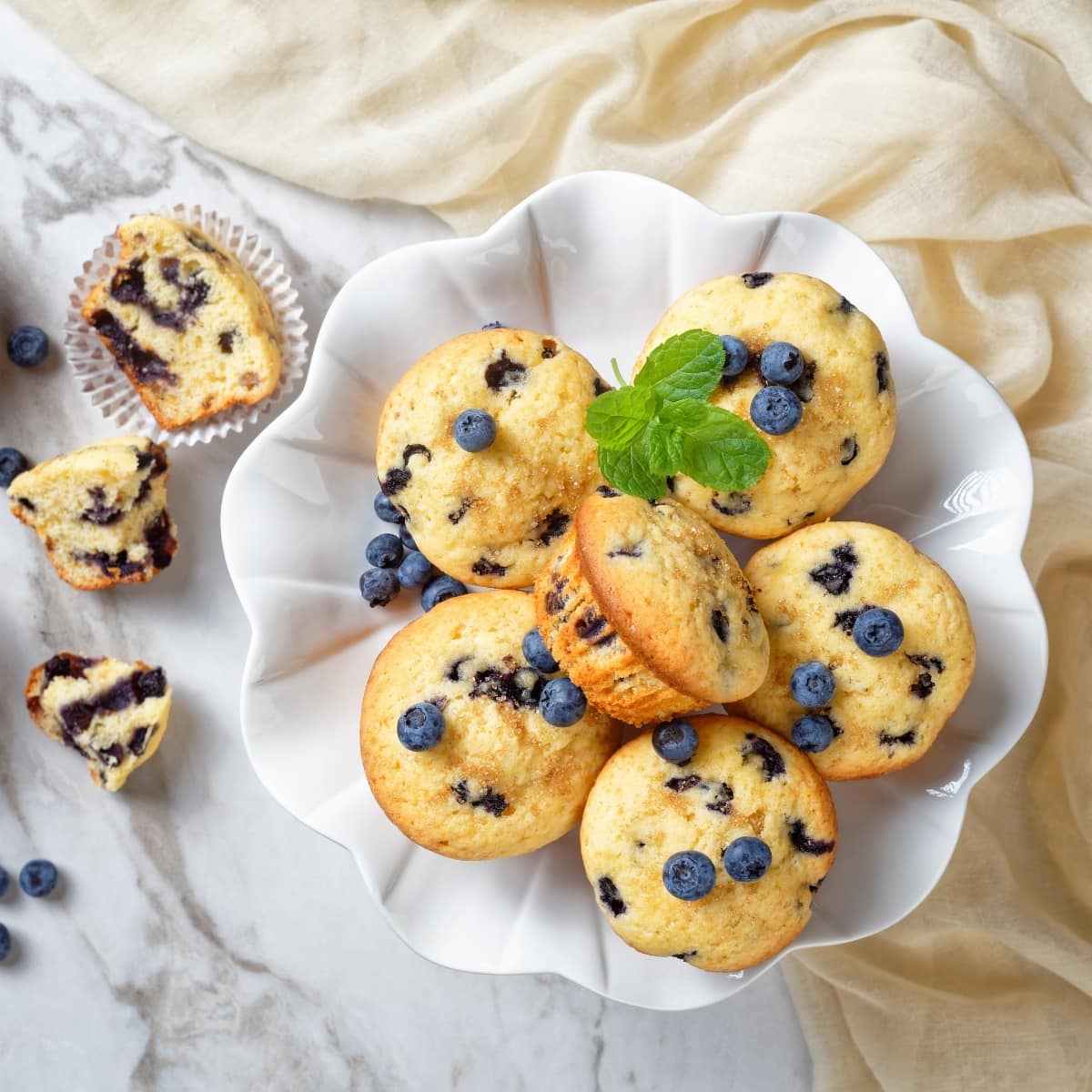 6 Jordan Marsh Blueberry Muffins on a Cake Tray with Another Muffing Sliced on the Side