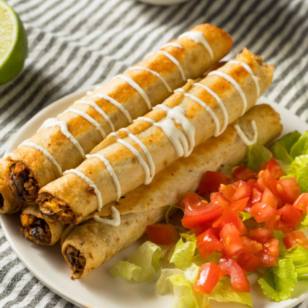 Homemade Flautas With Sliced Tomatoes and Cabbage, Drizzled With White Sauce