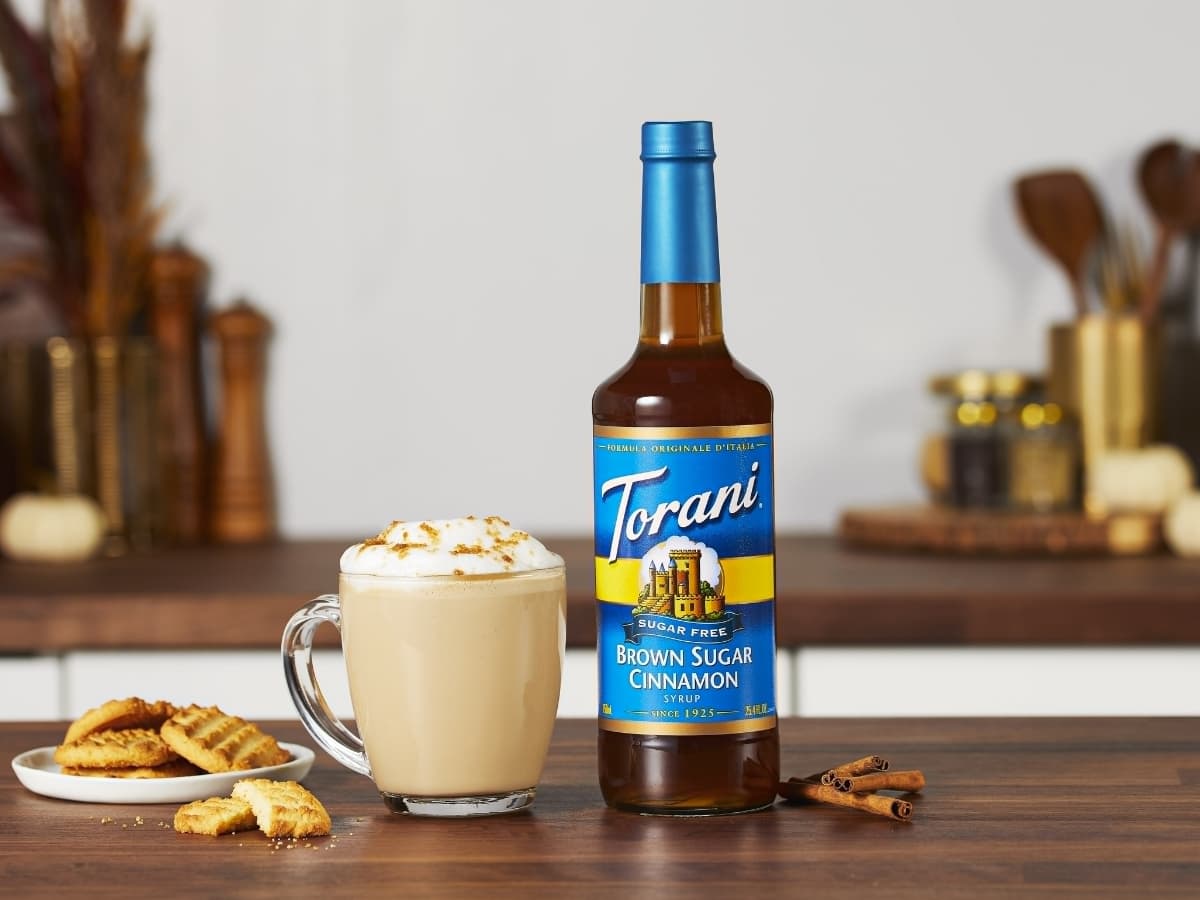 Mug of Latte, Bottle of Torani Brown Sugar Cinnamon Syrup, and Cookies on Plate on a Brown Wood Countertop