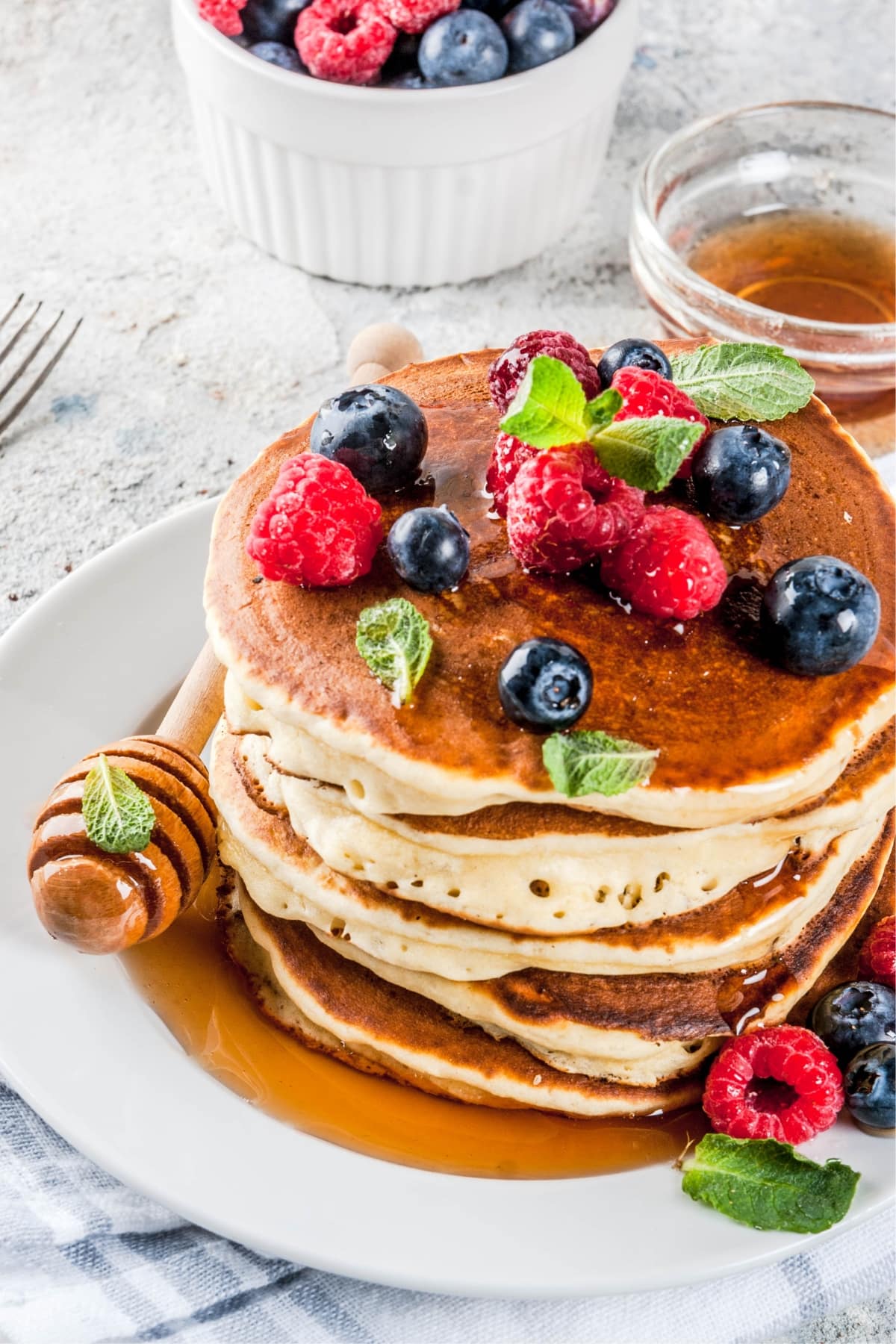 Plate stacked with homemade oat flour pancakes with fresh berries, honey, and mint leaves on top.