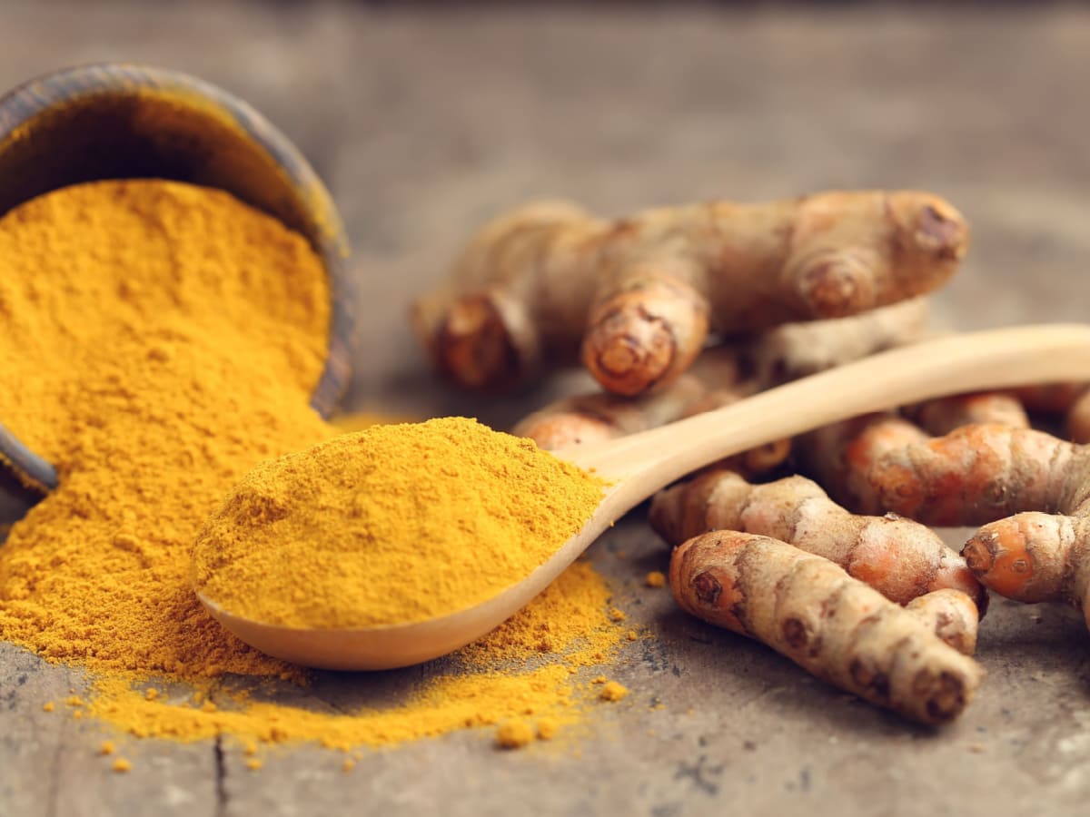 Turmeric Powder in a Spoon and Fresh Turmeric Root on a Wooden Table