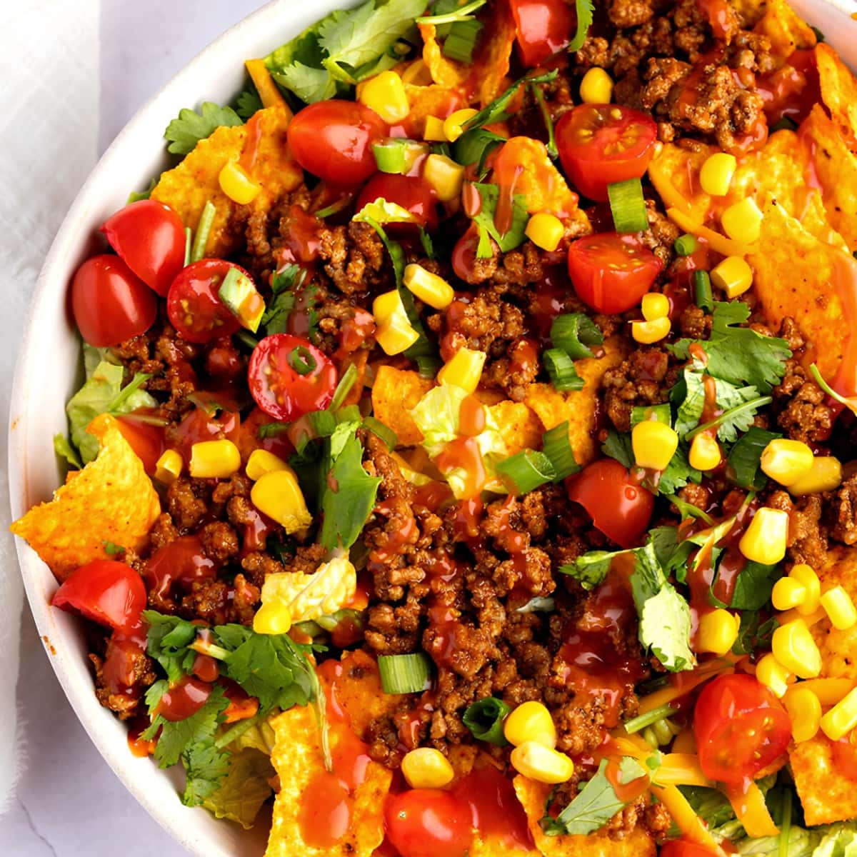 A bowl of Dorito Taco Salad, with beef, sliced tomato cherries, corn, chips garnished with chopped onions and cilantro