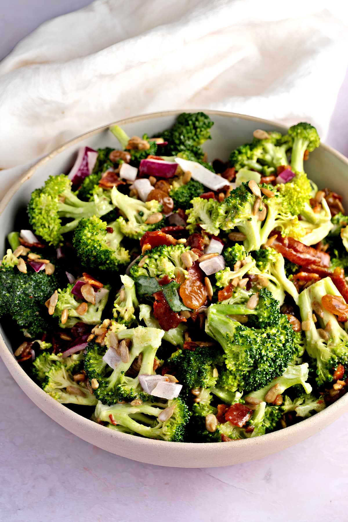 Bowl of broccoli salad with crumbled bacon, raisins, red onions and sunflower seed nuts.