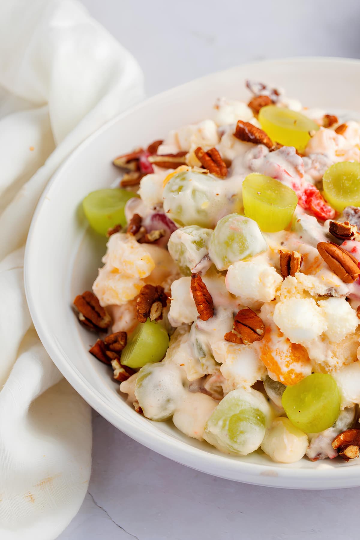 Christmas fruit salad with grapes, marshmallows, cherries and pecan nuts on a white bowl. 