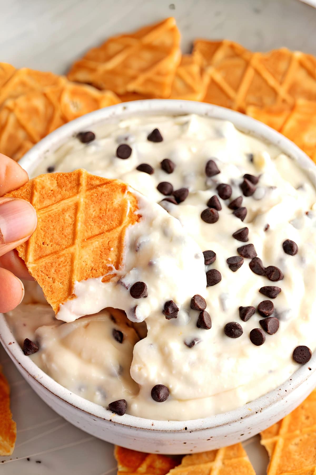 Waffle cone wafer being dipped in Cannoli Dip. Mini Chocolate chips on top.