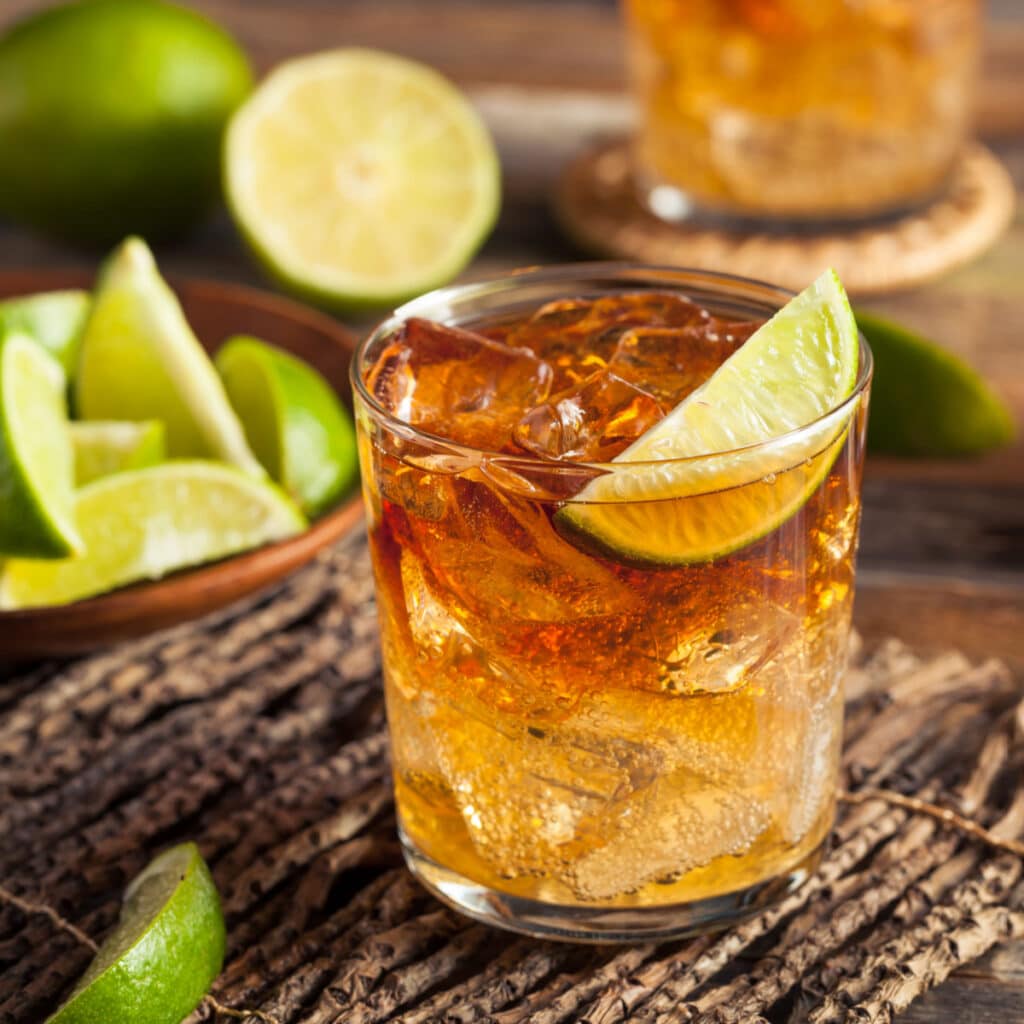 Glass of Dark and Stormy Cocktail filled with ice, garnished with green lime wedge