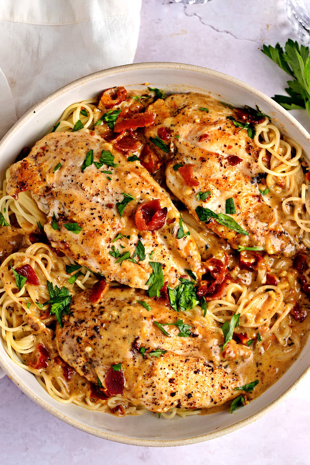 Top view of Marry Me Chicken dish on a bowl with pasta bacon and chopped herbs. 