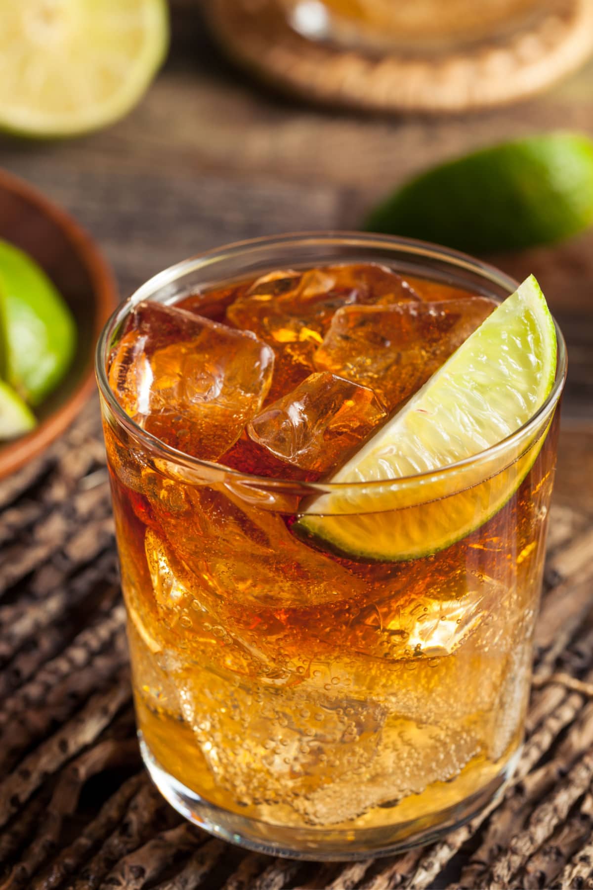 Dark and Stormy Cocktail in a glass filled with ice, garnished with a slice of a green lime