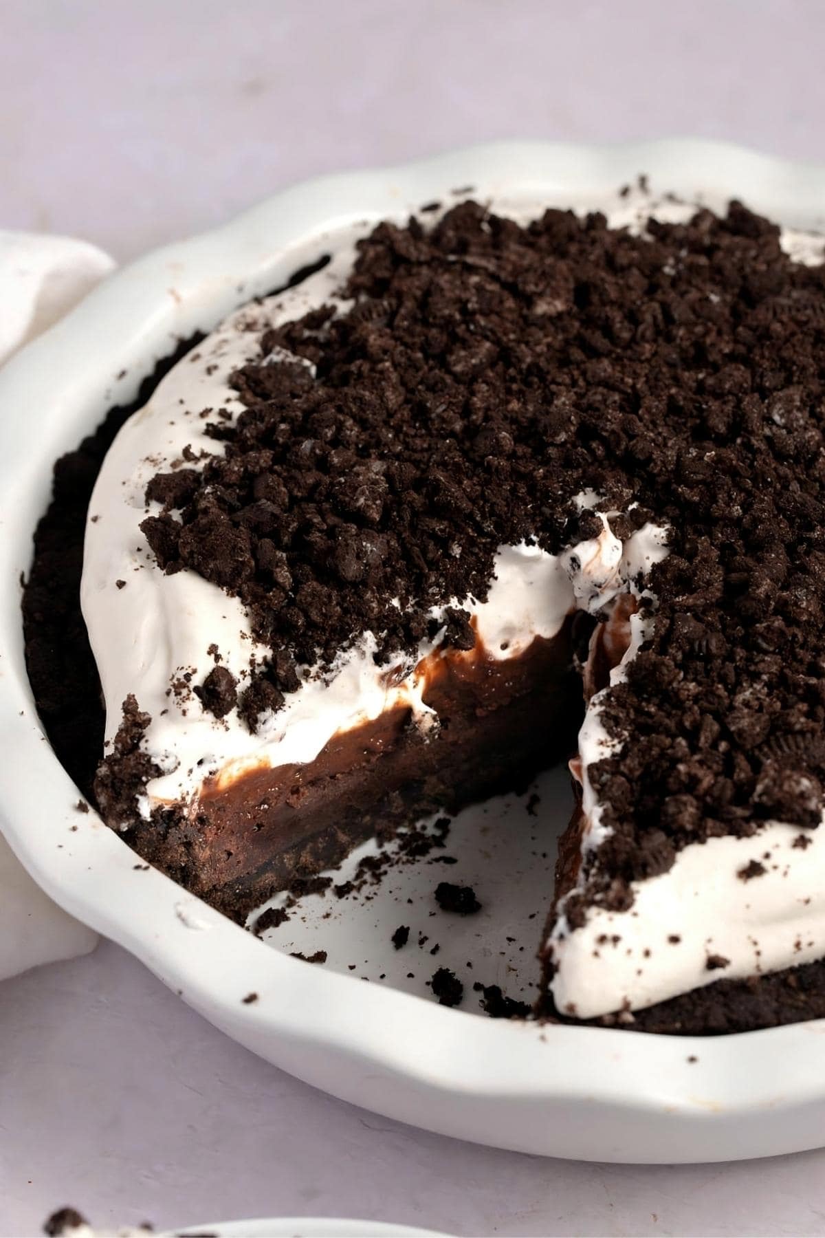Mississippi  mud pie with a slice taken out of it, served on a white bowl topped with crumbled oreo. 