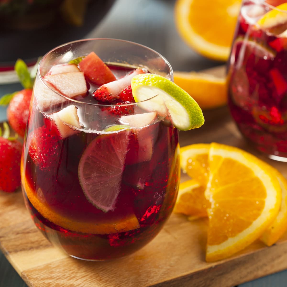 Glass of Red Sangria with fresh strawberries garnished with a green lemon wheel slice, slices of oranges in the  on a wooden board