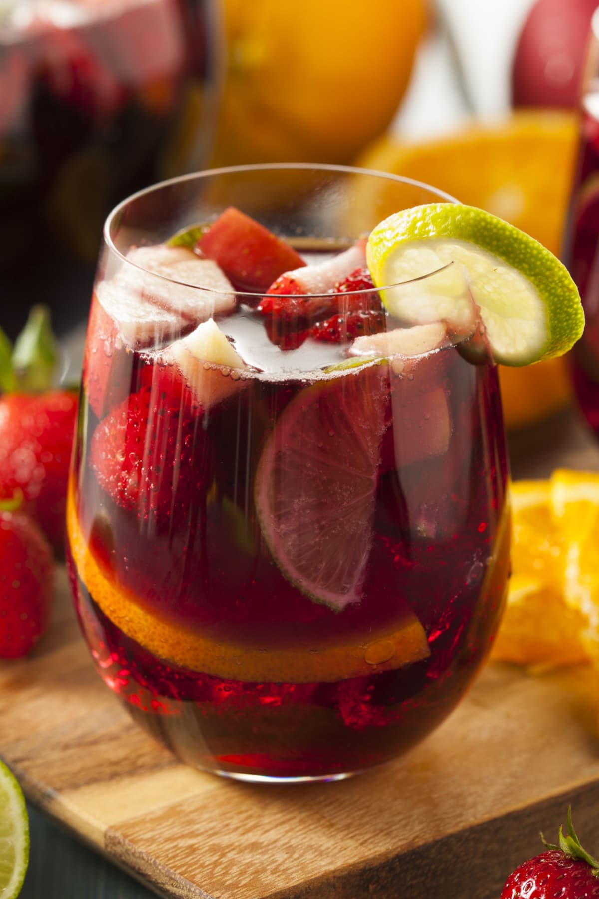 The Best Red Sangria (Easy Recipe) featuring A glass of Red Sangria with slices of fresh apples, oranges, and strawberries and a slice of lime wedge. 