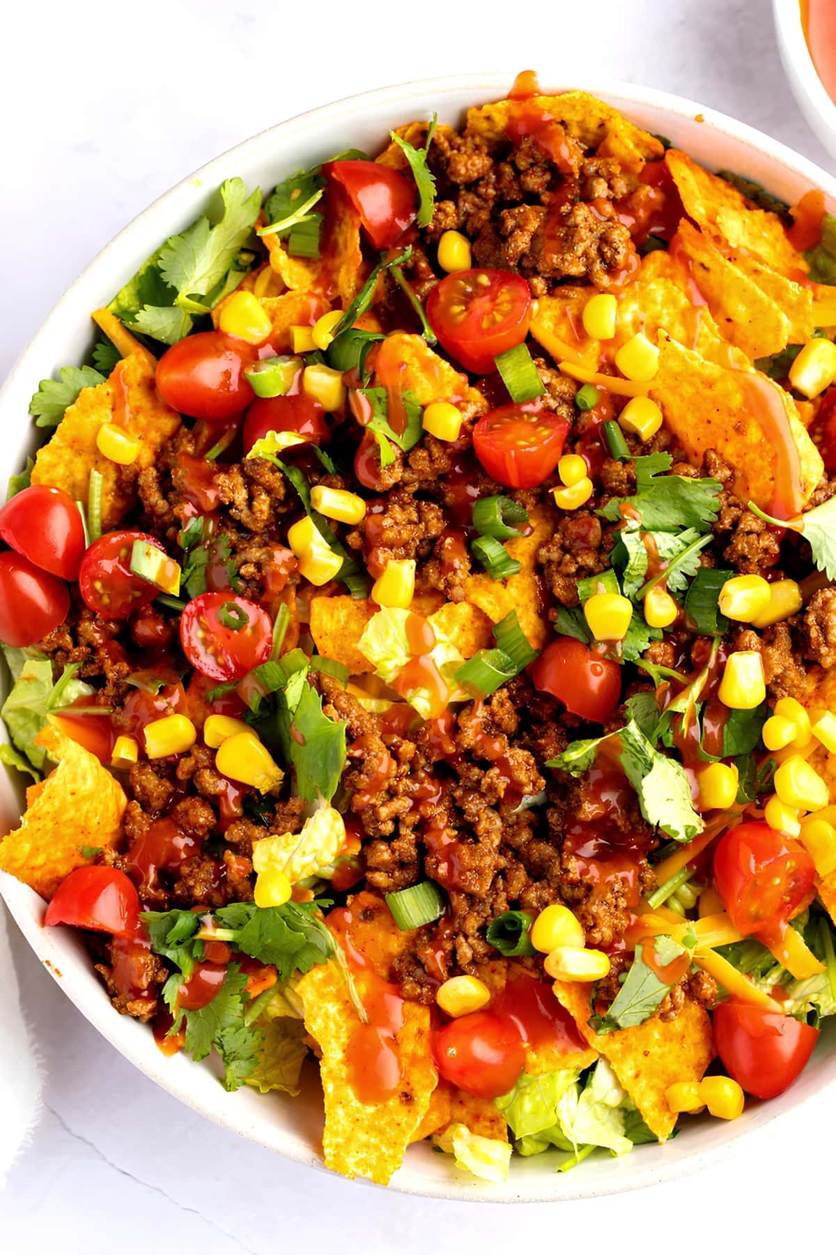 Top view of a bowl of Dorito Taco Salad, with beef, tomatoes and corn, bell pepper and greens.