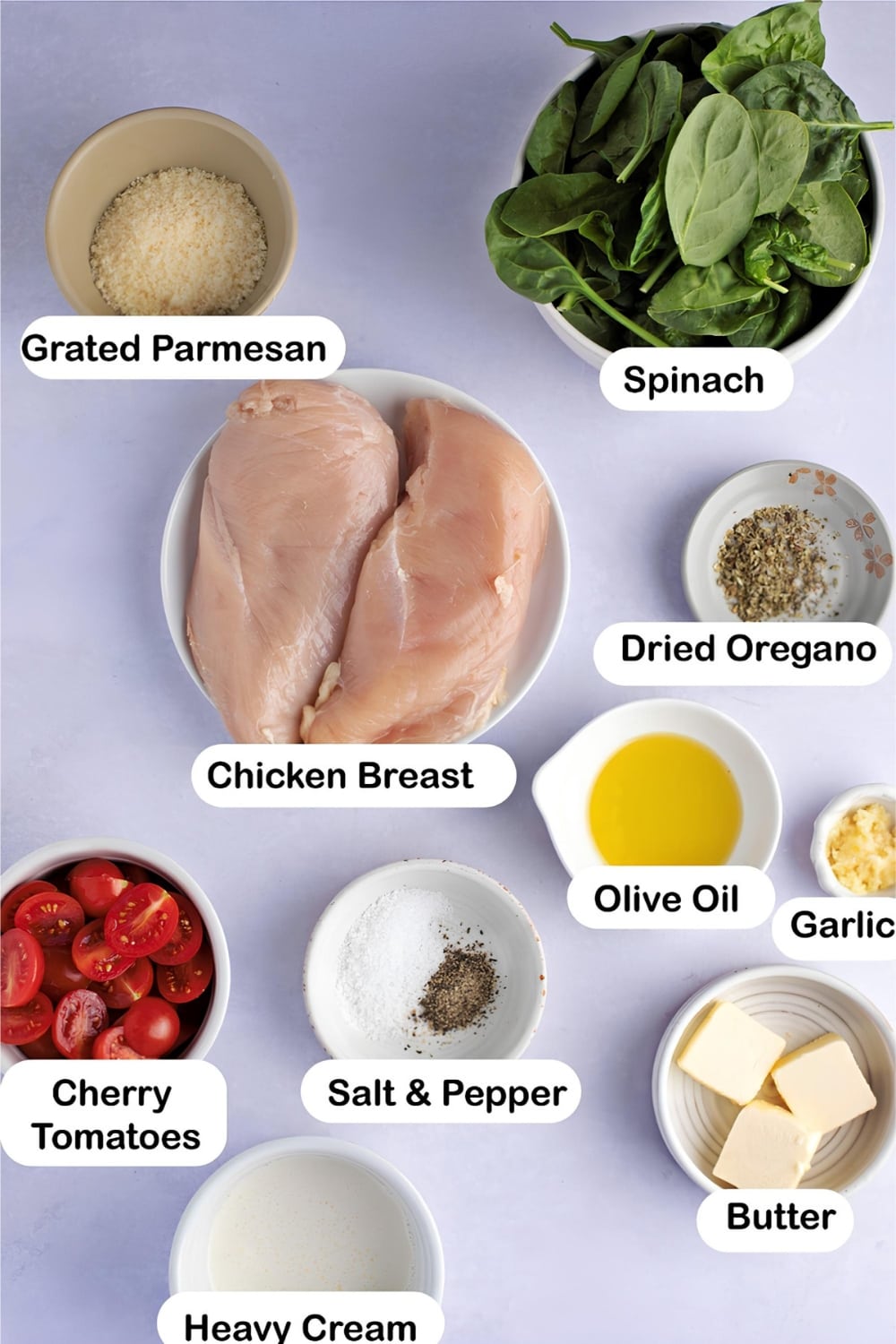 Tuscan Chicken ingredients on bowls, grated parmesan cheese. spinach. chicken breast, dried oregano, cherry tomatoes. olive oil, minced garlic, butter, heavy cream, salt and pepper