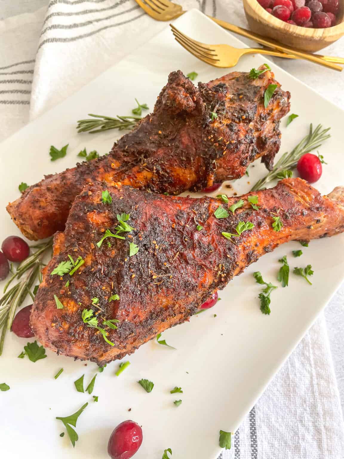 Two Air Fryer Turkey Legs on a plate garnish with parsley, rosemary and cranberries