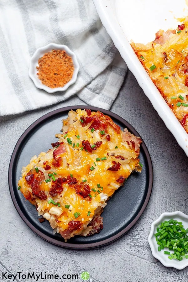 Slice of Breakfast Casserole with bacon, hash browns, sweet onion, and cheese on a saucer garnished with spring onions