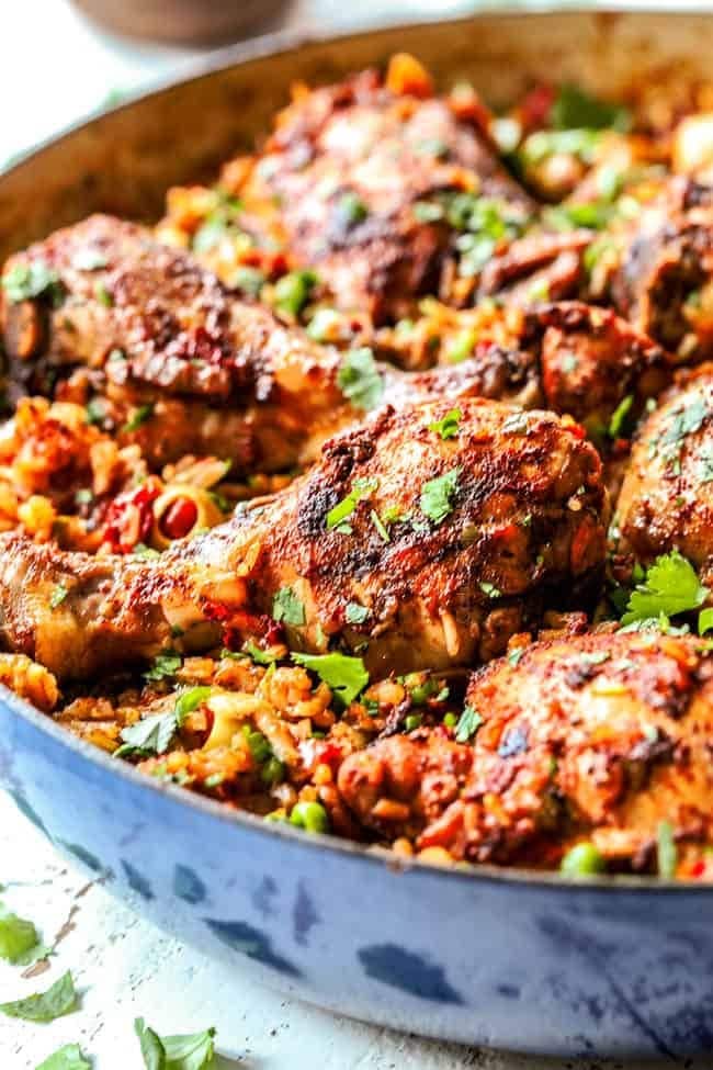 Arroz con Pollo with tomatoes, bell peppers, onions, peas, and olives in pan.