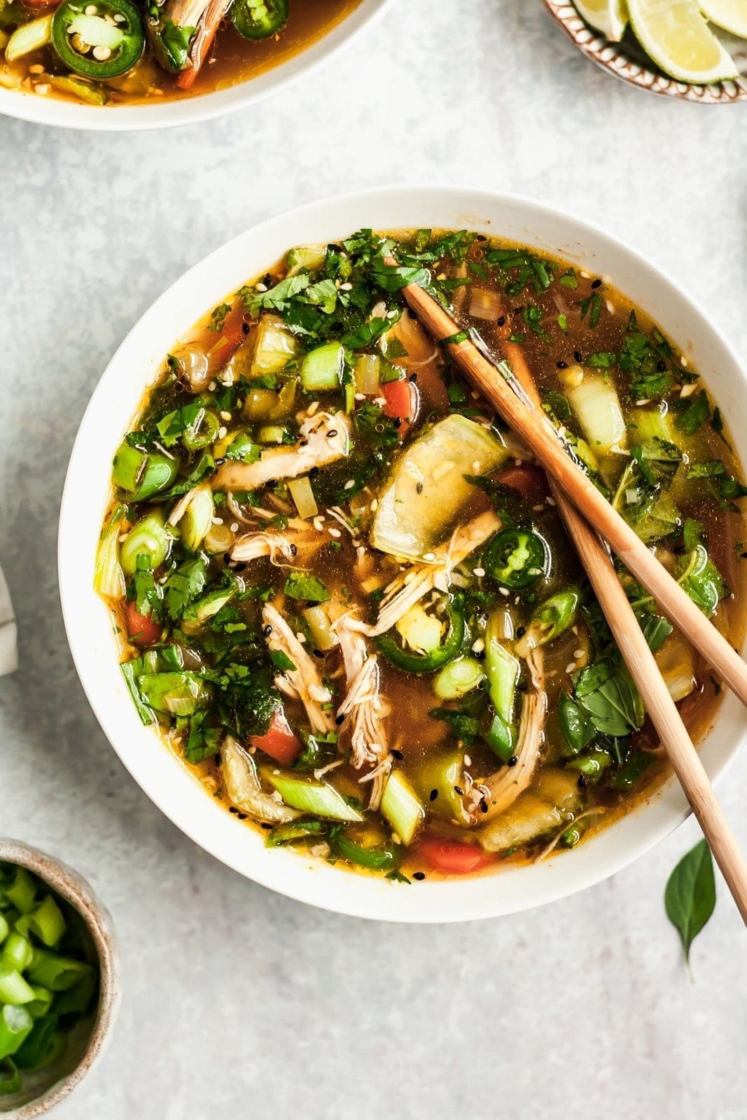 A bowl of Asian-inspired chicken soup in a bowl with garlic, ginger, lemongrass, cilantro, mint, and basil.