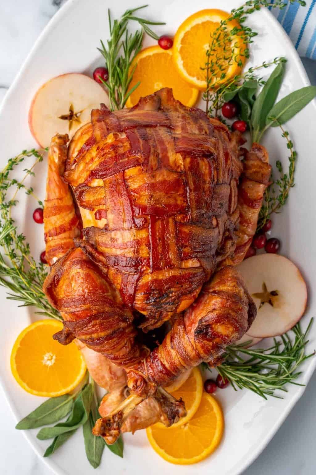 Bacon-Wrapped Turkey garnished with slices of oranges and apples with herbs on a oval plte