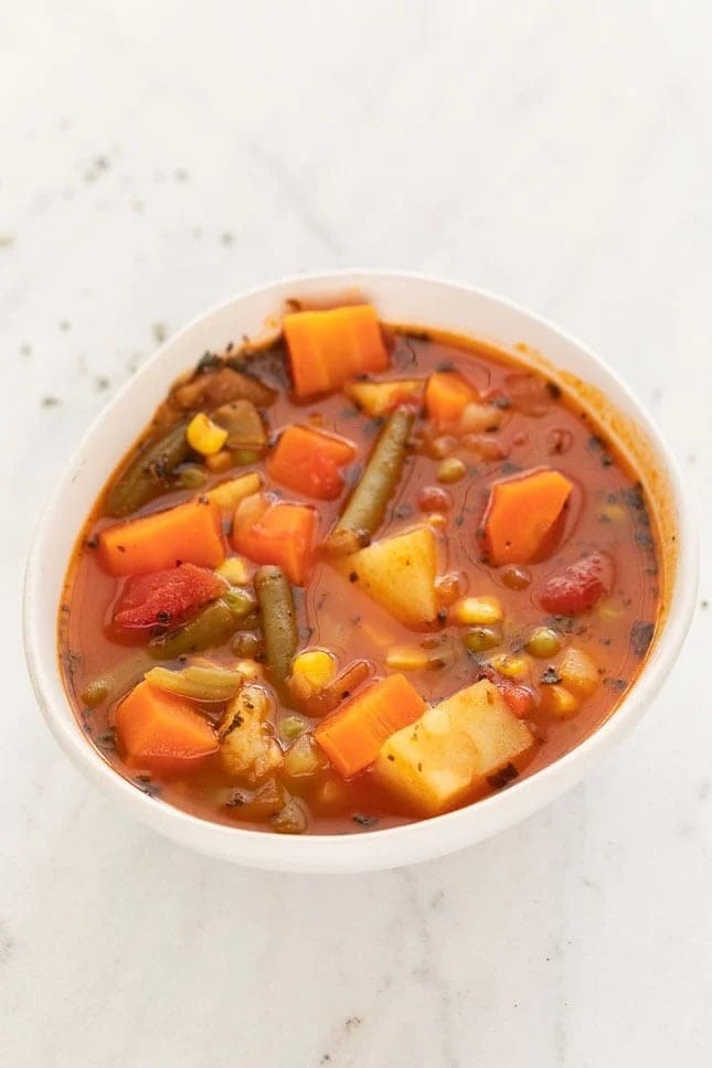 Bowl of homemade Vegetable Soup with carrots, potatoes, celery stalk, corn kernels, green peas and beans