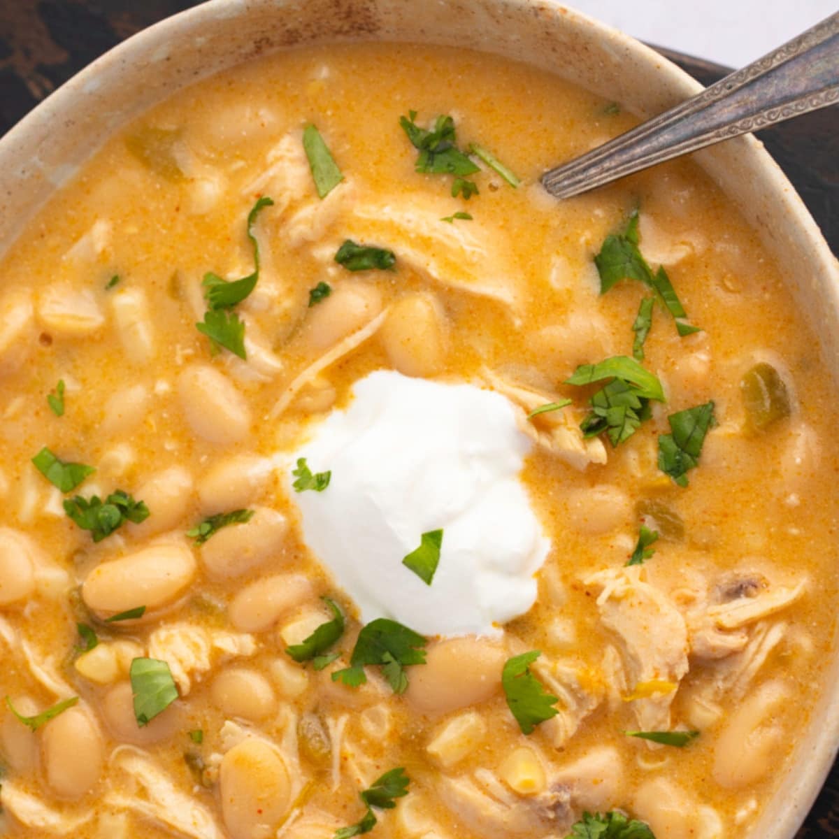 Top view of a bowl of white chicken chili garnished with chopped parsley leaves. 