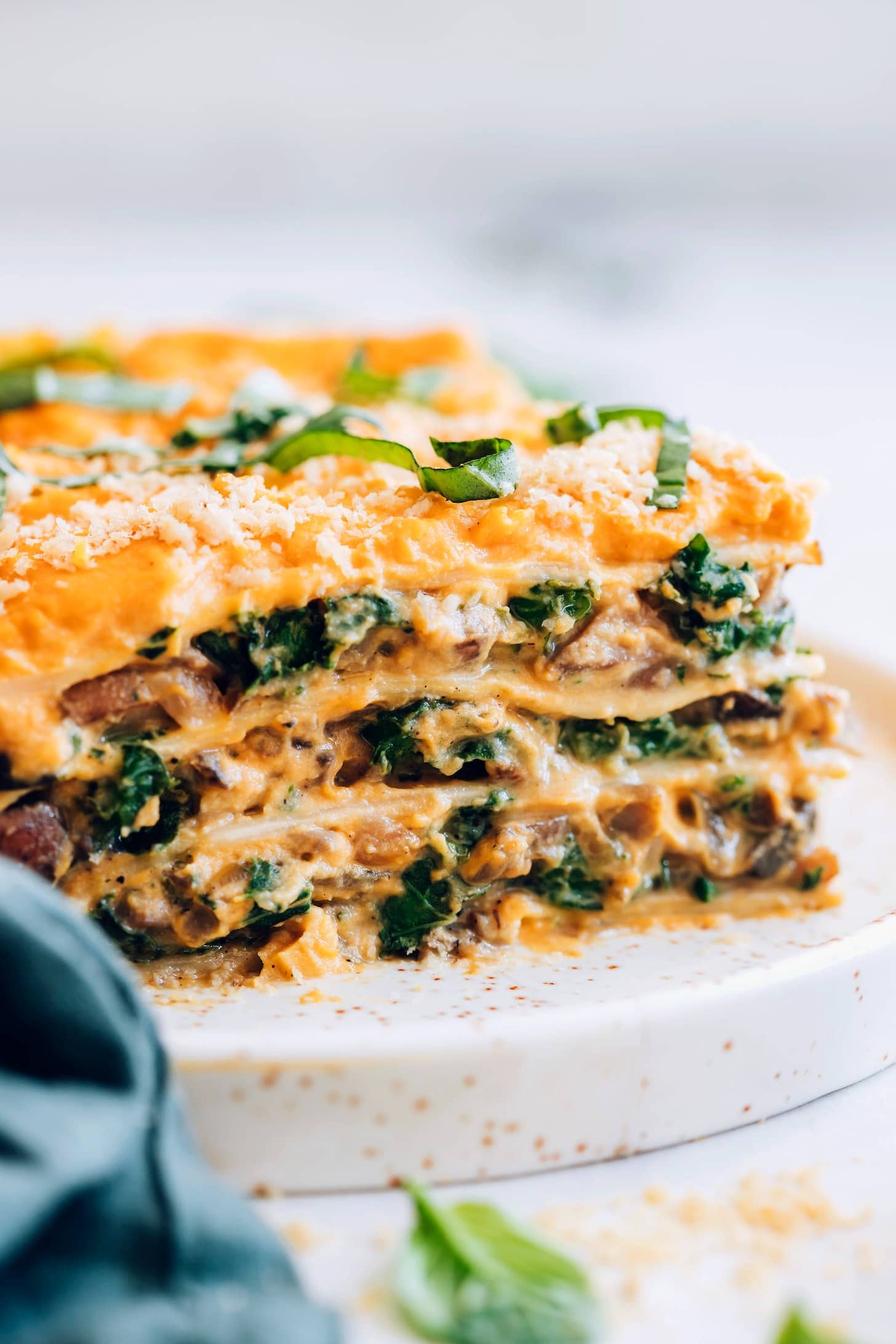 A slice of vegan lasagna with spinach and mushrooms served on a white plate.