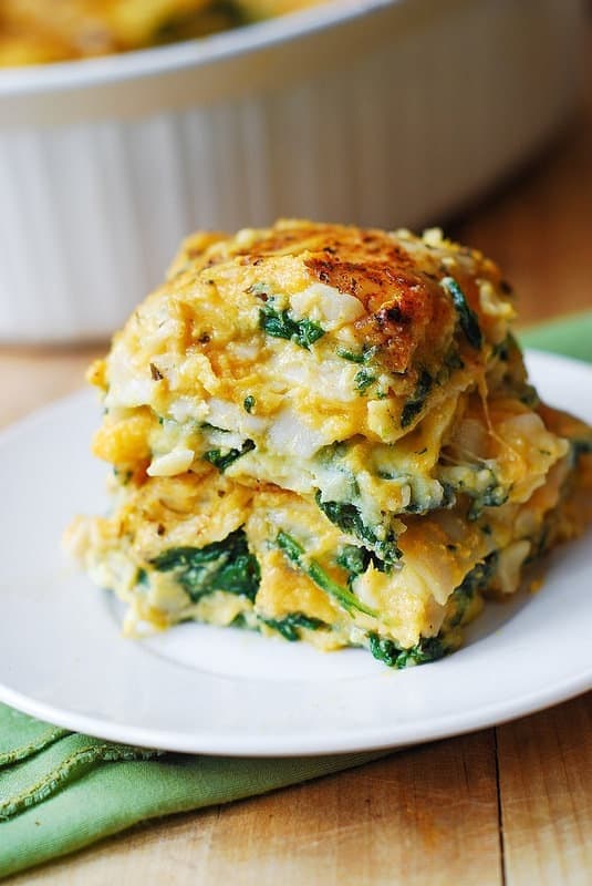 A slice of butternut squash and spinach lasagna made with stuffed with ricotta, parmesan, and mozzarella served on a white plate. 