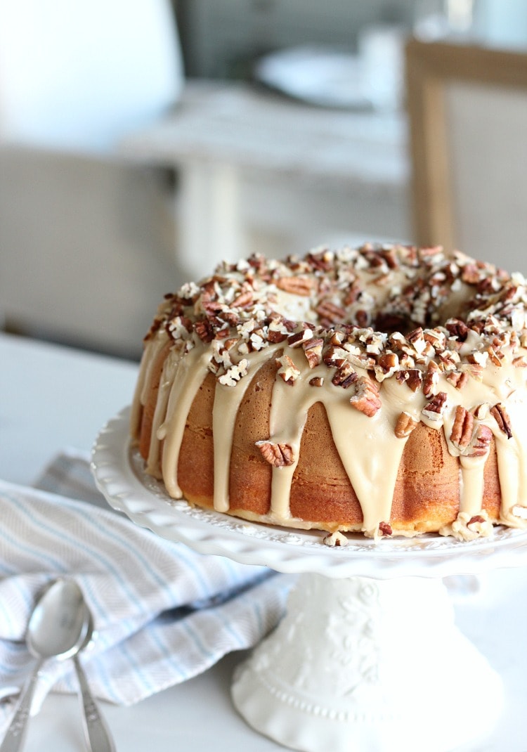 Caramel Pecan Bundt cake on a cake tray topped with dripping caramel glaze and chopped pecan nuts.  
