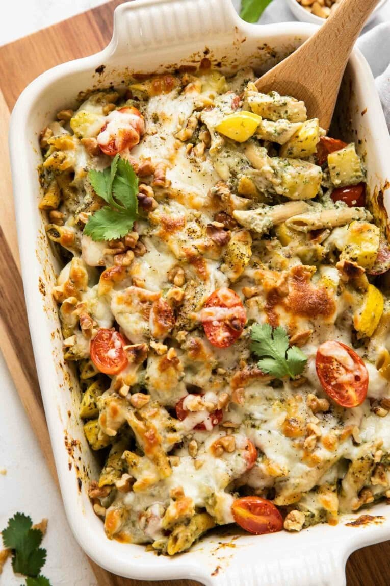 Top view of chicken pesto pasta bake on a white dish made with cheese, pasta, and a few veggies. 