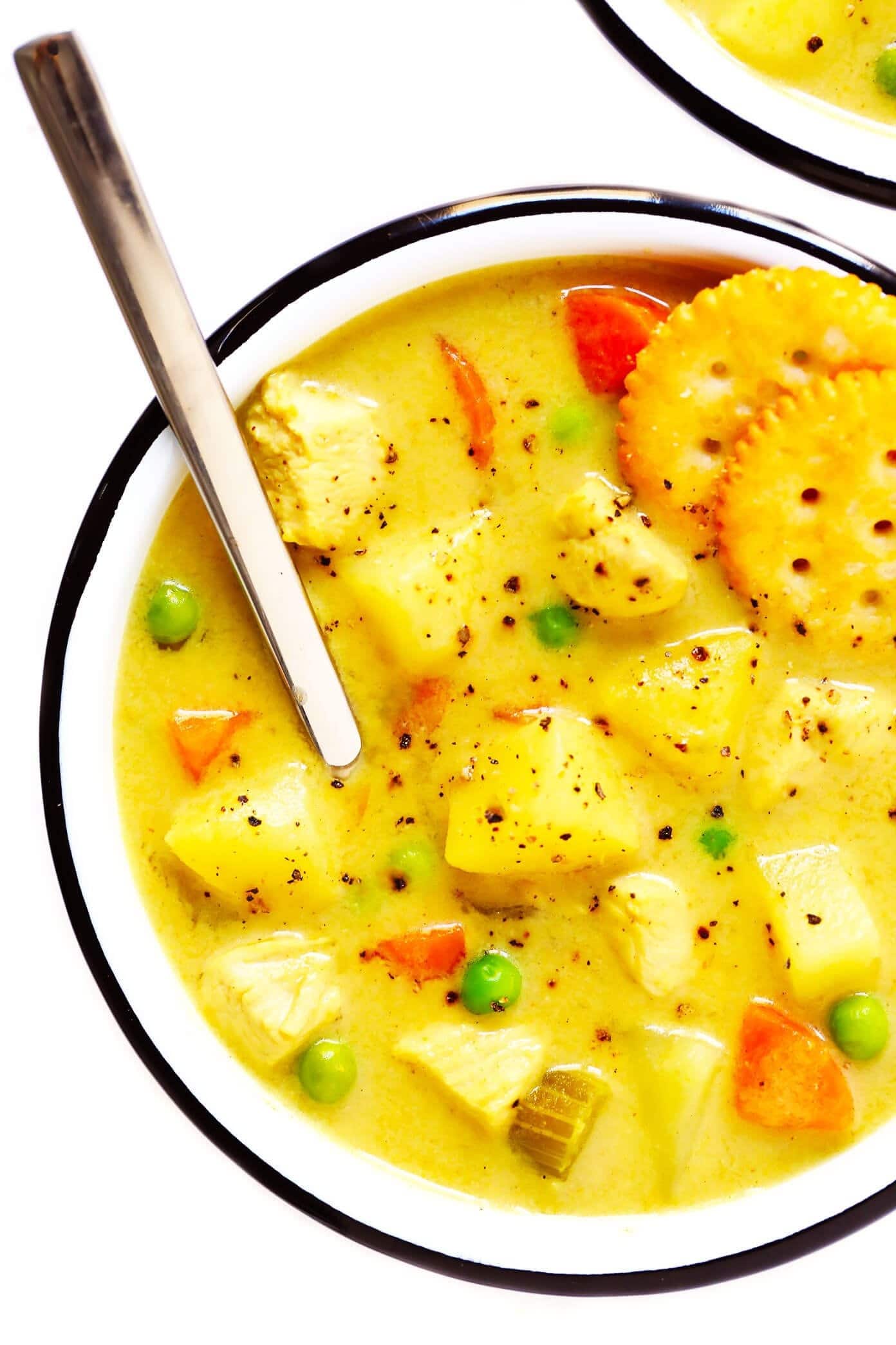 Top view of a bowl of chicken curry soup with crackers and spoon. 