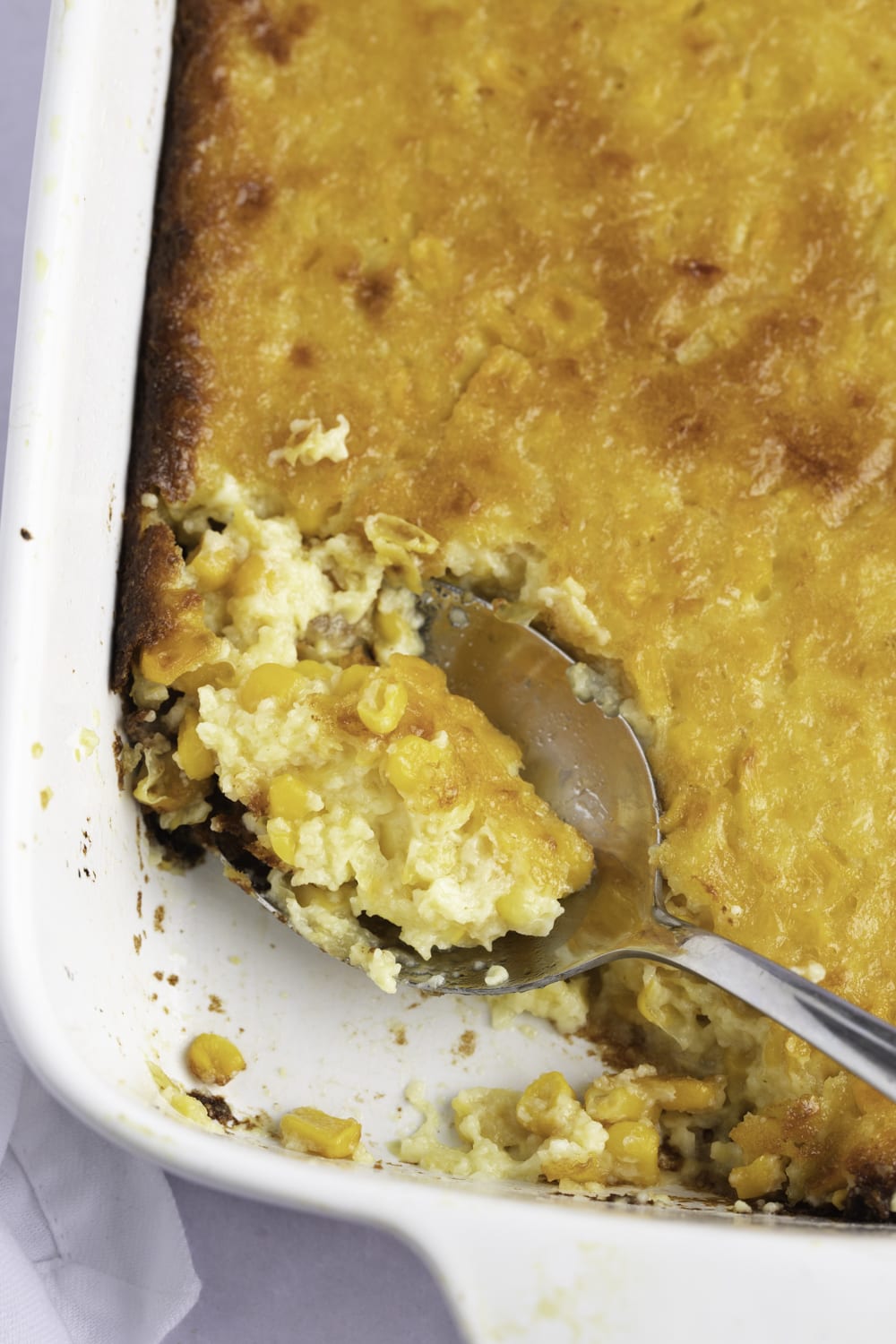 Spoon scooping creamy corn pudding in a casserole. 