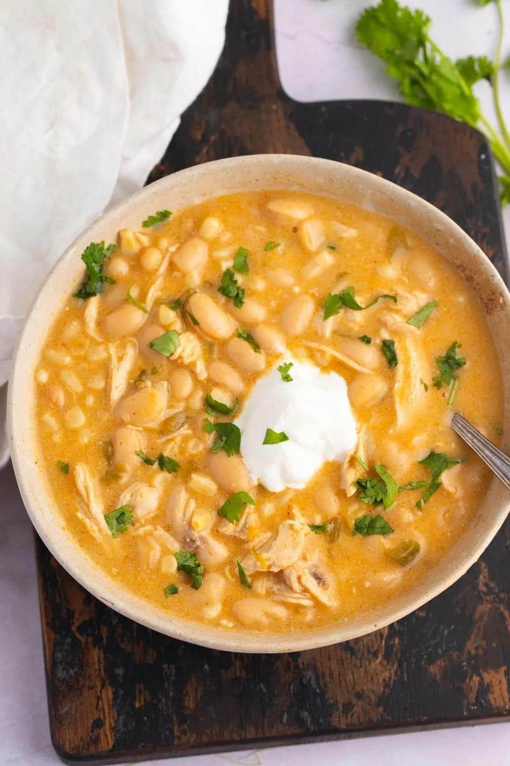 Chicken chili with beans, stock and chicken meat topped with cream served on a white bowl.