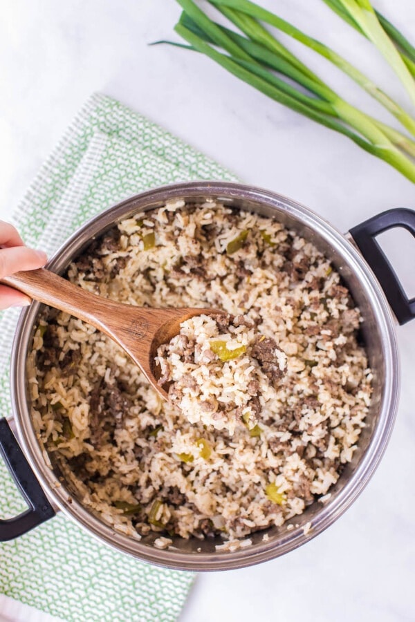 Top view of a pot with dirty rice mixed with a wooden spoon ladle. 