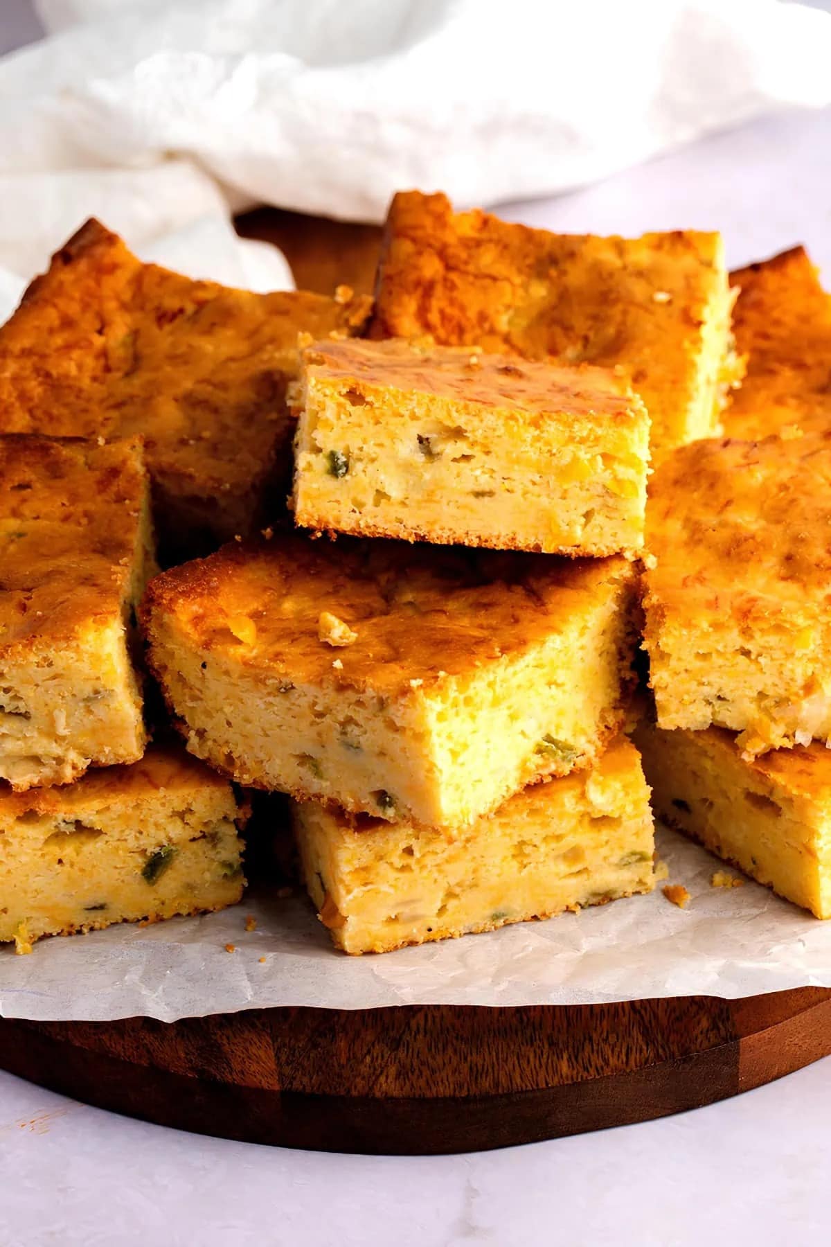 Stack of slices of Mexican cornbread on a round wooden cutting board.