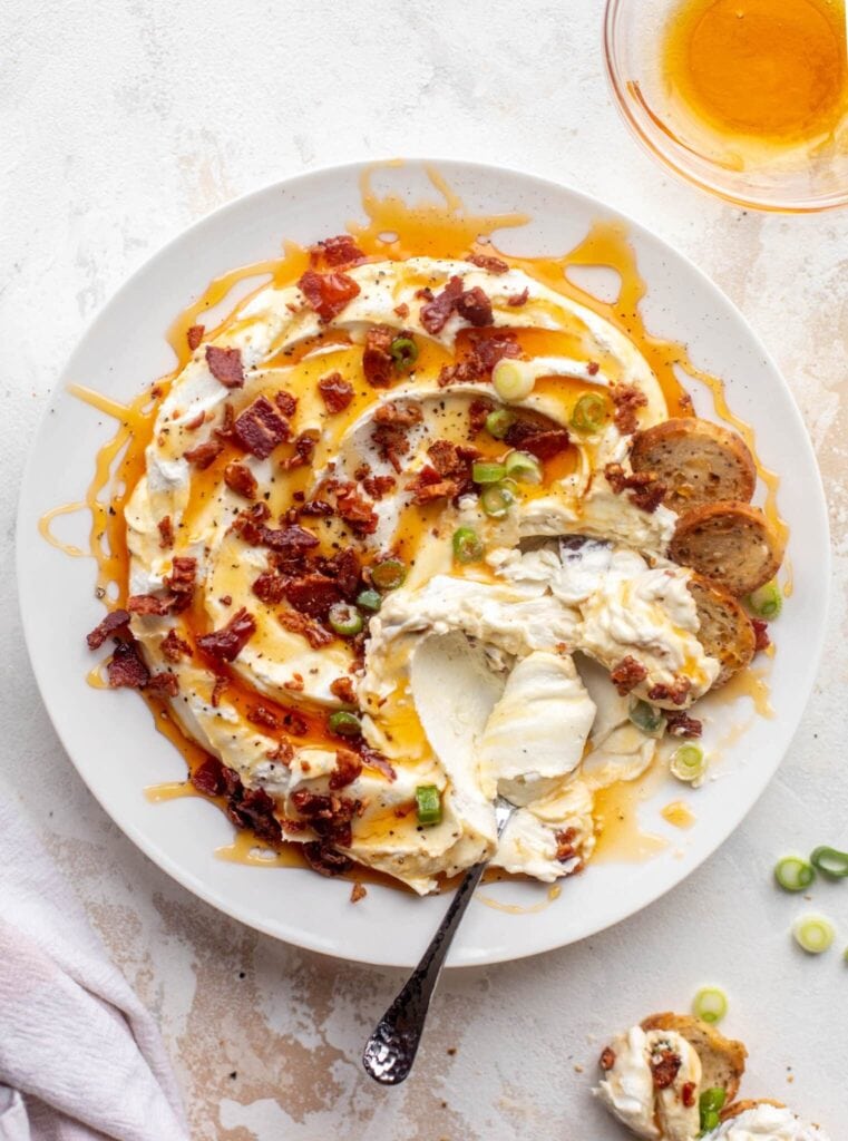 Whipped goat cheese dip with bacon and honey on a plate with spoon. 