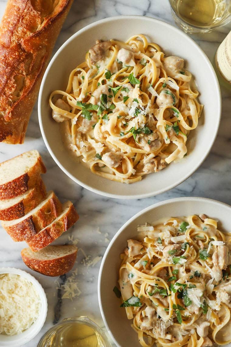 Two servings of chicken alfredo served on a plate with sliced bread. 