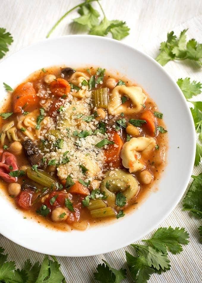 Bowl of homemade Instant Pot Tortellini Vegetable Soup with chopped carrots, celery, tomatoes, rosemary, mushrooms, baby spinach and garnished with basil leaves and grated cheese